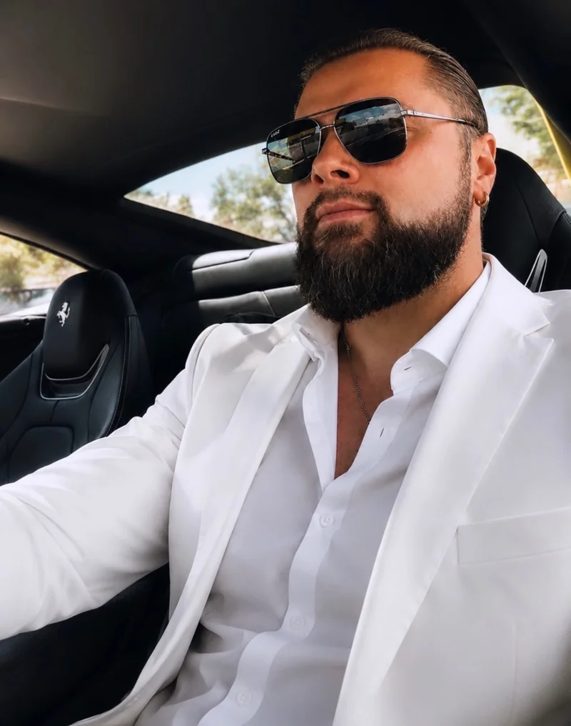 Mark Pugachev in a white suit seated in a vehicle